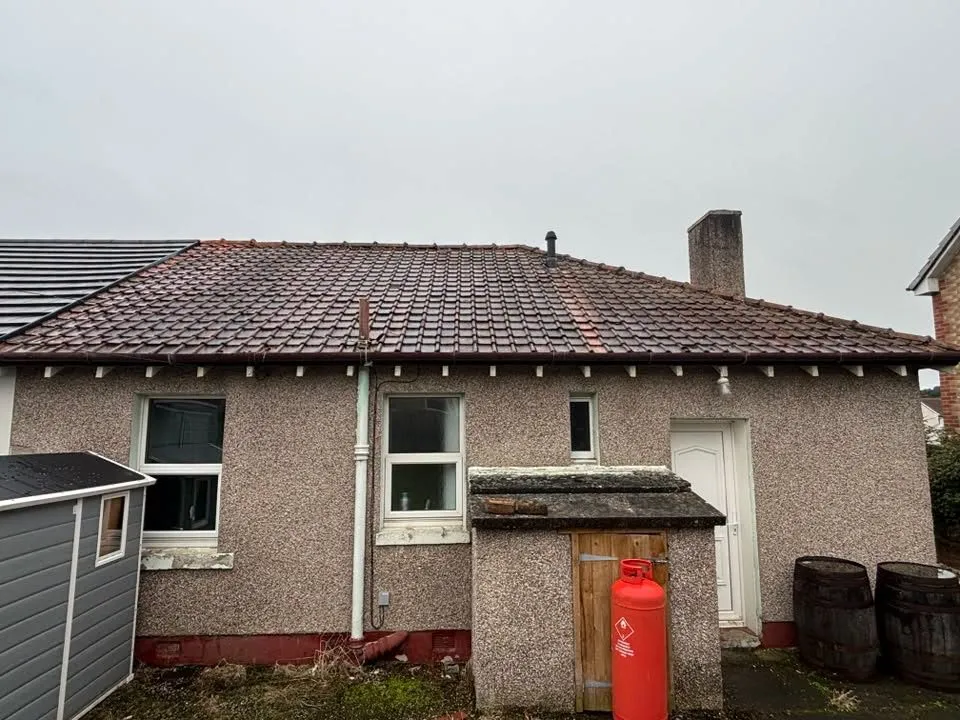 Back of a bungalow with a moss-darkened tiled roof before cleaning