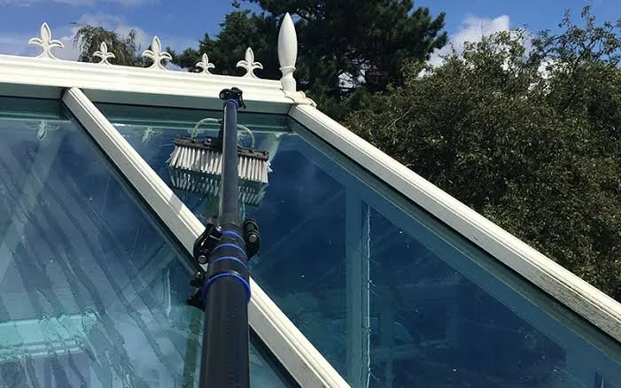Brush head on a water-fed pole cleaning a glass conservatory roof and white uPVC frames
