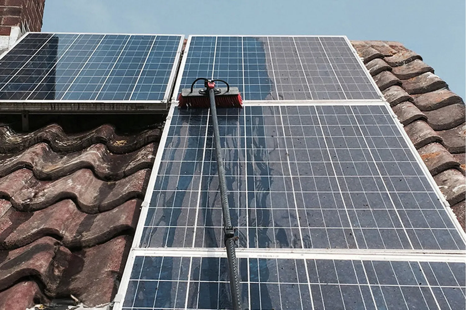 Brush head on a water-fed pole cleaning dirty solar panels on a tiled roof